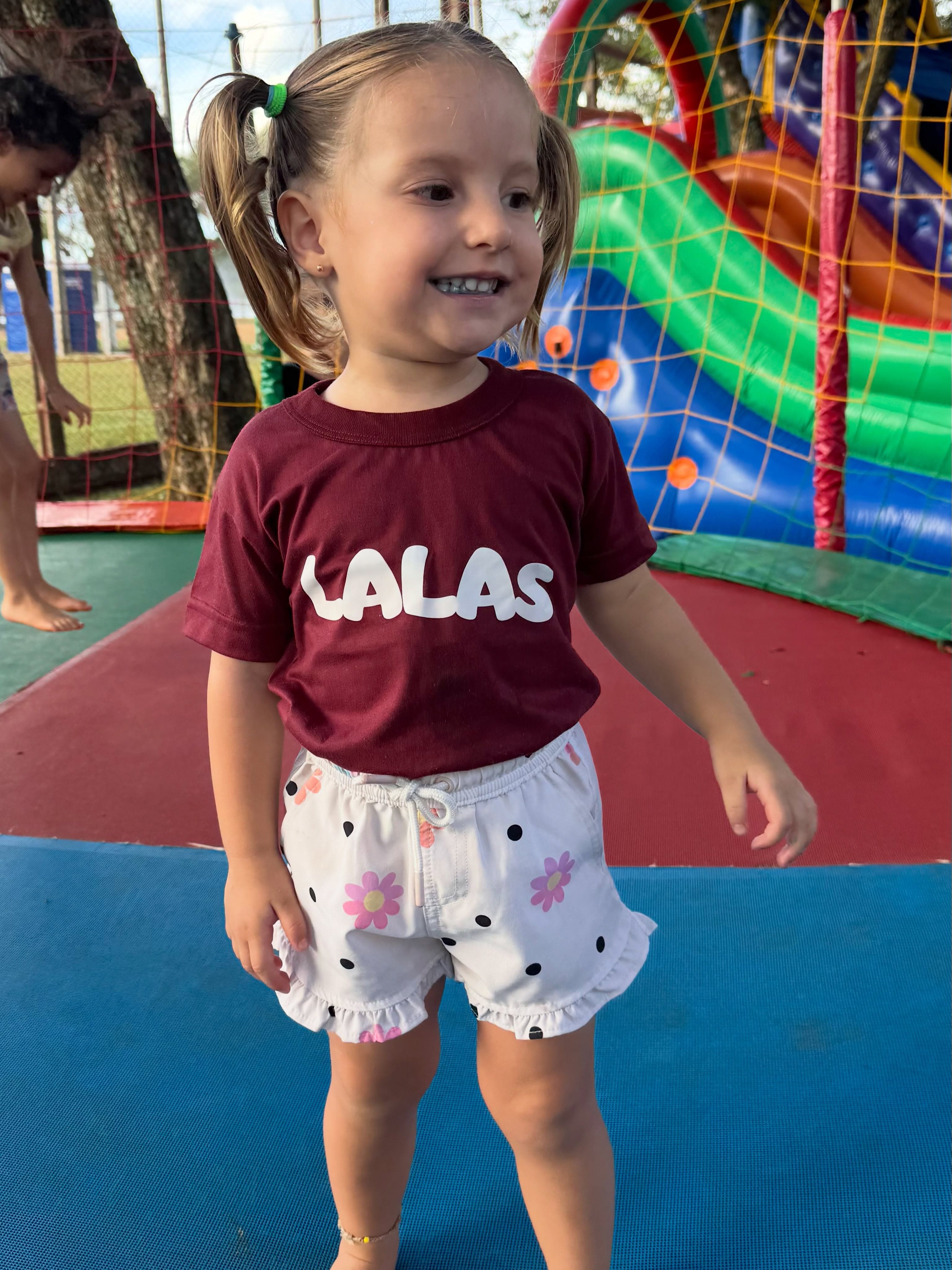 Criança com camiseta da Lalás em frente a um tobogã inflável